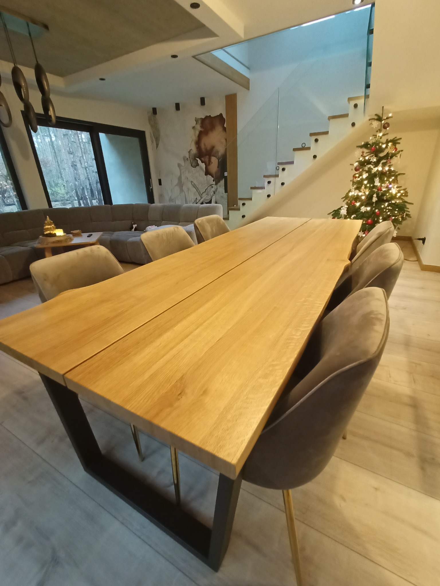 Stół z litego drewna z metalowymi nogami w nowoczesnym wnętrzu z schodami i choinką. Jasne drewno blatu kontrastuje z ciemnymi nogami stołu.