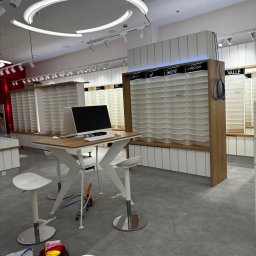 Instant Clean - Wnętrze sklepu optycznego z pustymi półkami na okulary, biurkiem z komputerem i widocznymi akcesoriami do sprzątania podłogi. Przygotowanie do otwarcia.