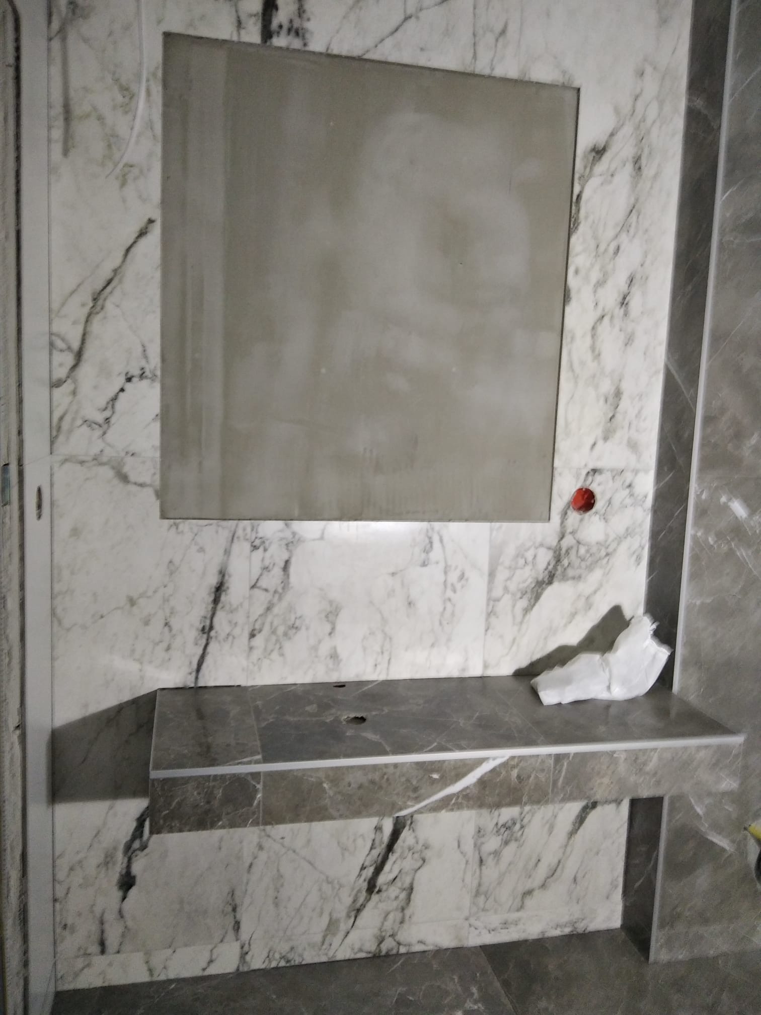 Łazienka w trakcie wykańczania: marmurowe płytki na ścianach, zamontowana umywalka z blatem z tego samego materiału, wnęka na lustro przygotowana do montażu.