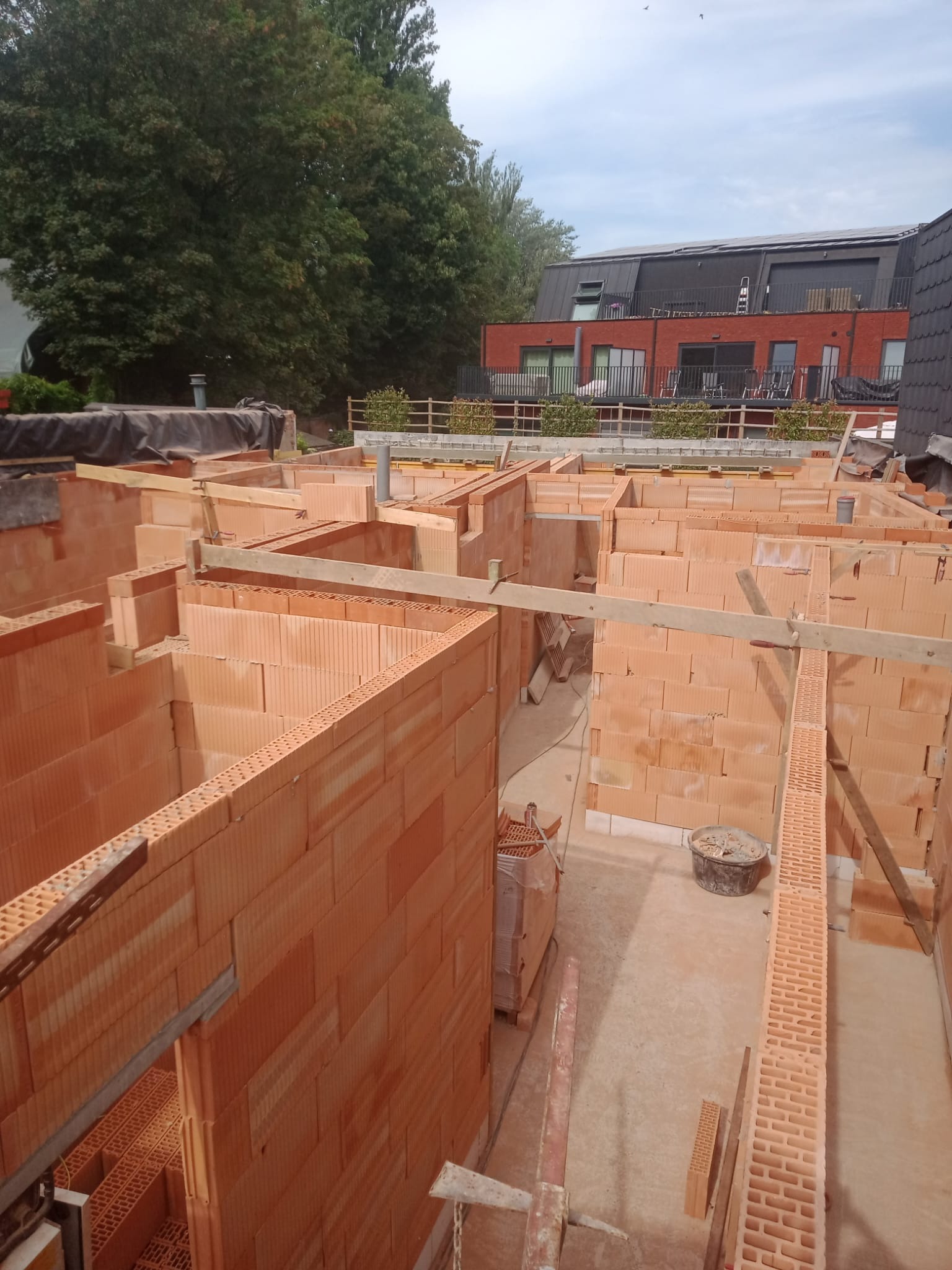 Wznoszenie ścian działowych z czerwonej cegły ceramicznej, widok z góry na wnętrze budynku w trakcie budowy, drewniane podpory i narzędzia budowlane w kadrze.