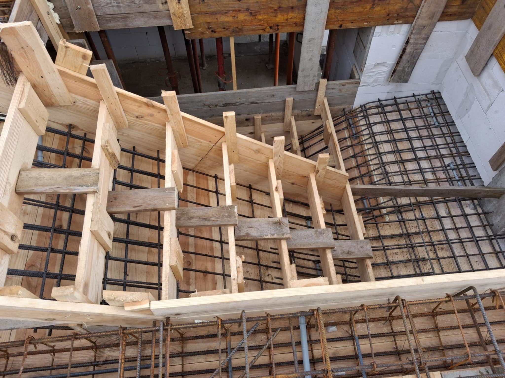 Szkielet schodów z drewnianym szalunkiem i zbrojeniem stalowym, widok z góry. Etap budowy, surowe materiały, detale konstrukcyjne.