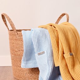 InUse sp z o o - Koszyk z naturalnego materiału wypełniony błękitnym i żółtym, teksturowanym materiałem, prawdopodobnie ręcznikami lub szlafrokami z metkami.