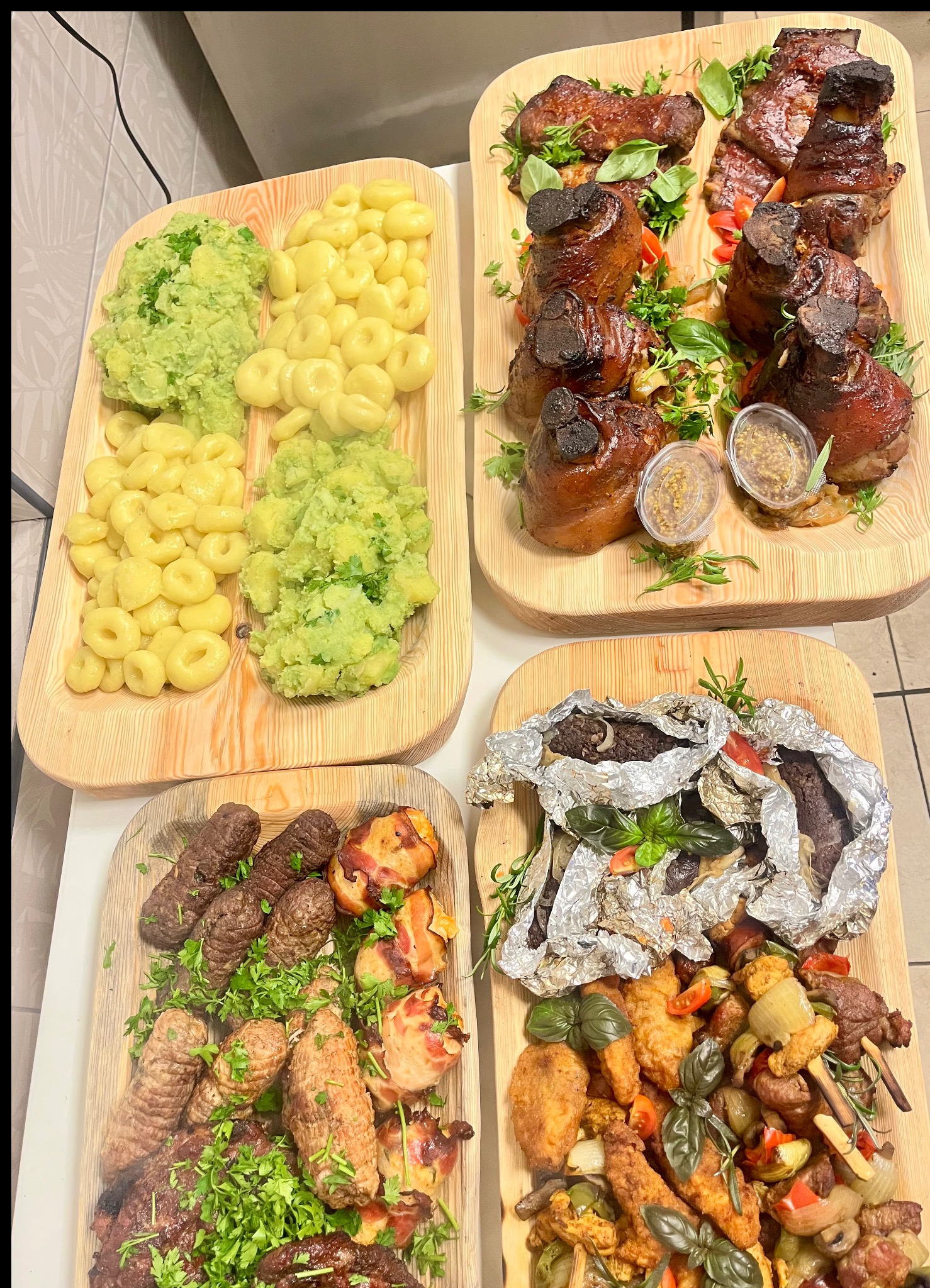 Bogaty wybór dań na drewnianych deskach: golonka, kaszanka w folii, kluski, puree, szaszłyki i mięsa, udekorowane ziołami. Idealne menu na imprezę.