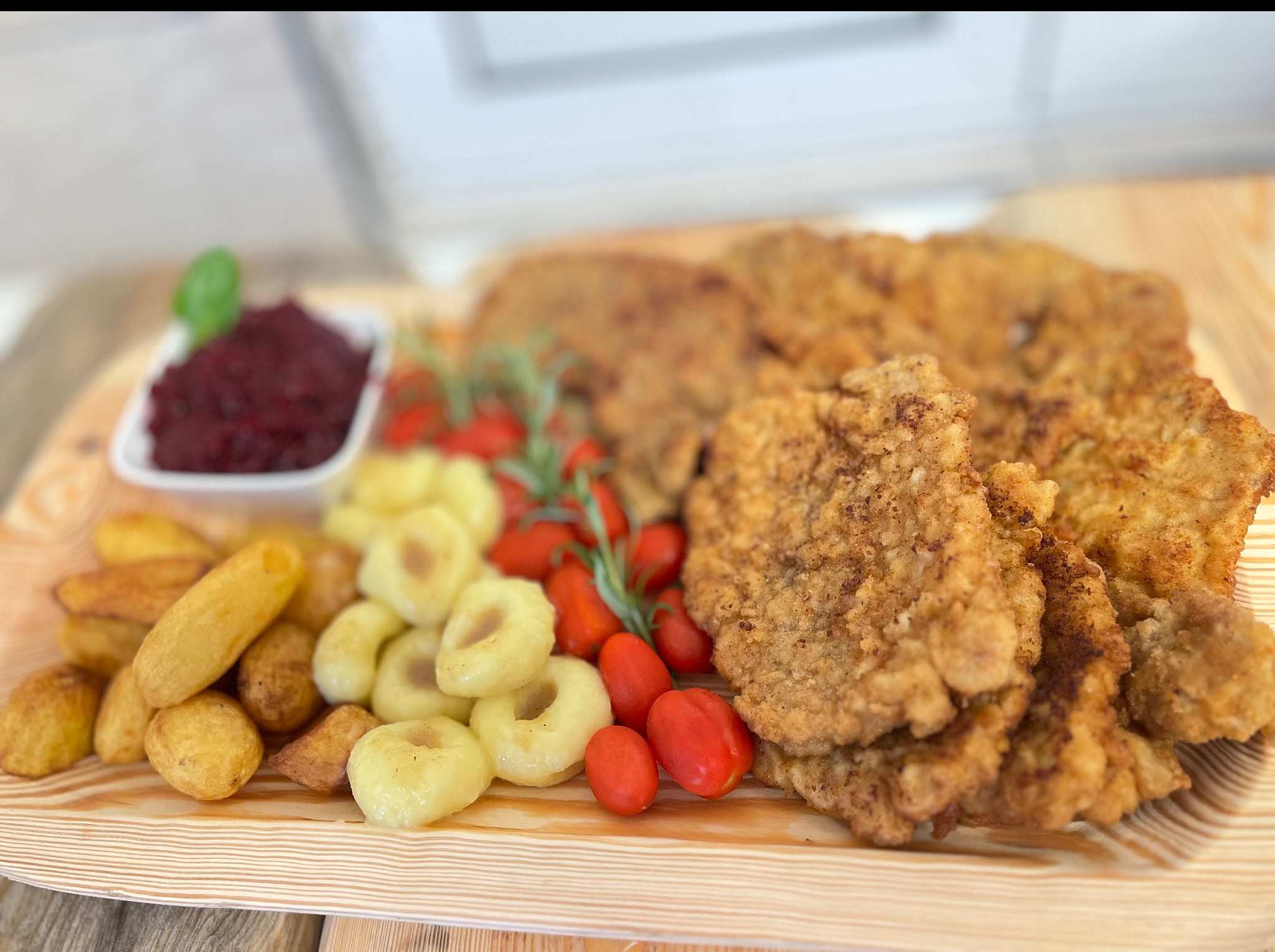 Tradycyjny obiad na drewnianej desce: kotlety schabowe, ziemniaki, kluski śląskie, buraczki z bazylią i pomidorki koktajlowe z rozmarynem. Domowy posiłek.