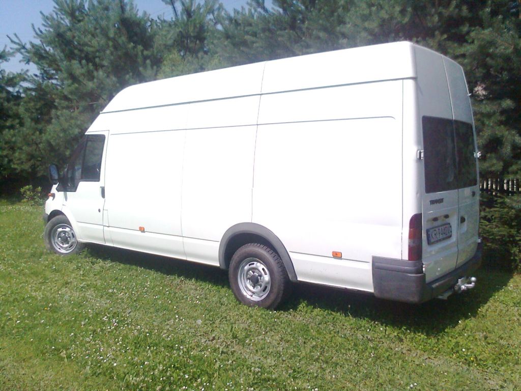 Biały, wysoki furgon na trawiastym terenie, widok z tyłu i boku, z widoczną tablicą rejestracyjną KR 9440V.