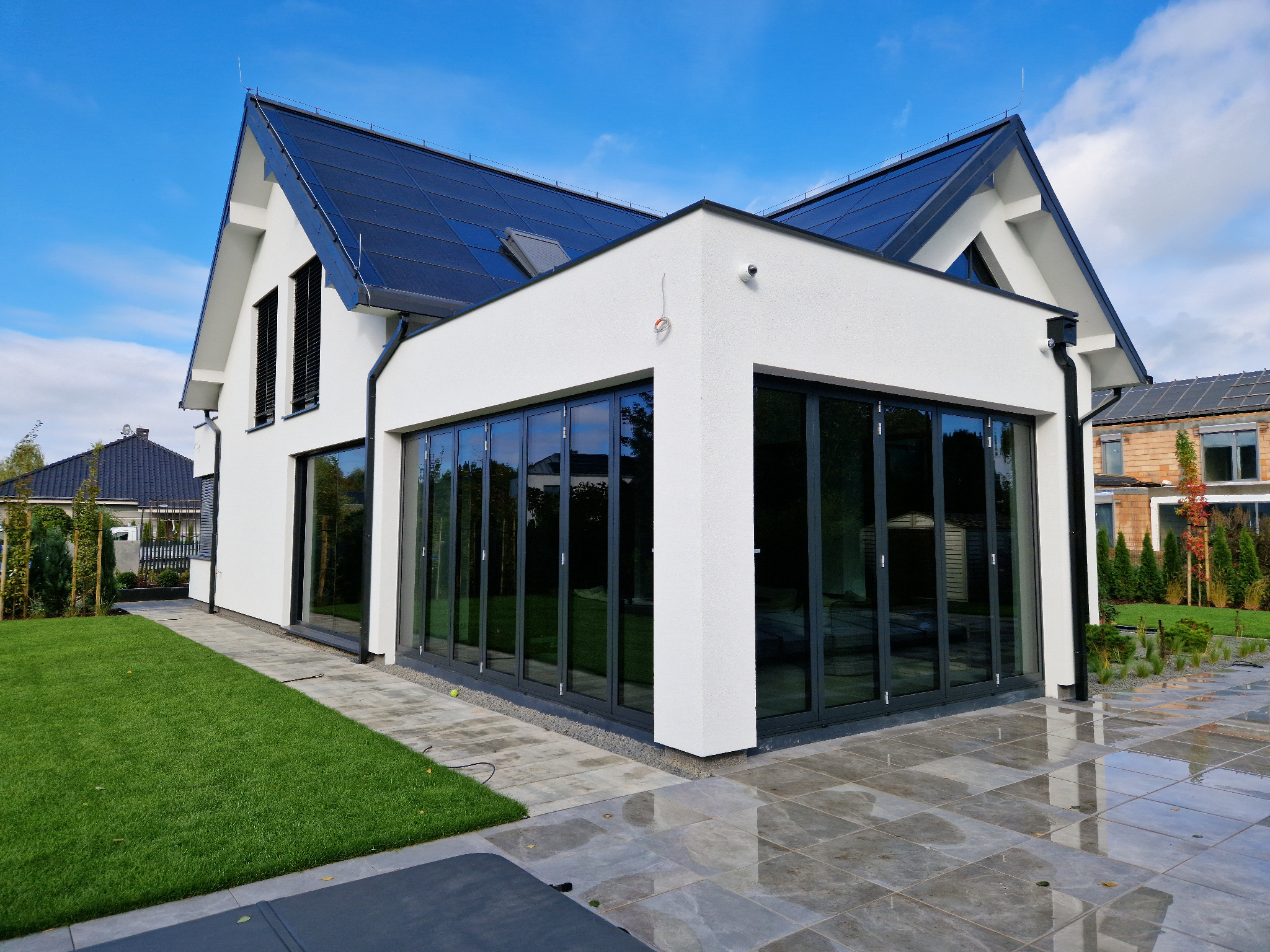 Nowoczesny dom z dużymi, przesuwnymi oknami w Obornikach. Eleganckie wykończenie i zadbany ogród. Widok z zewnątrz, w słoneczny dzień.