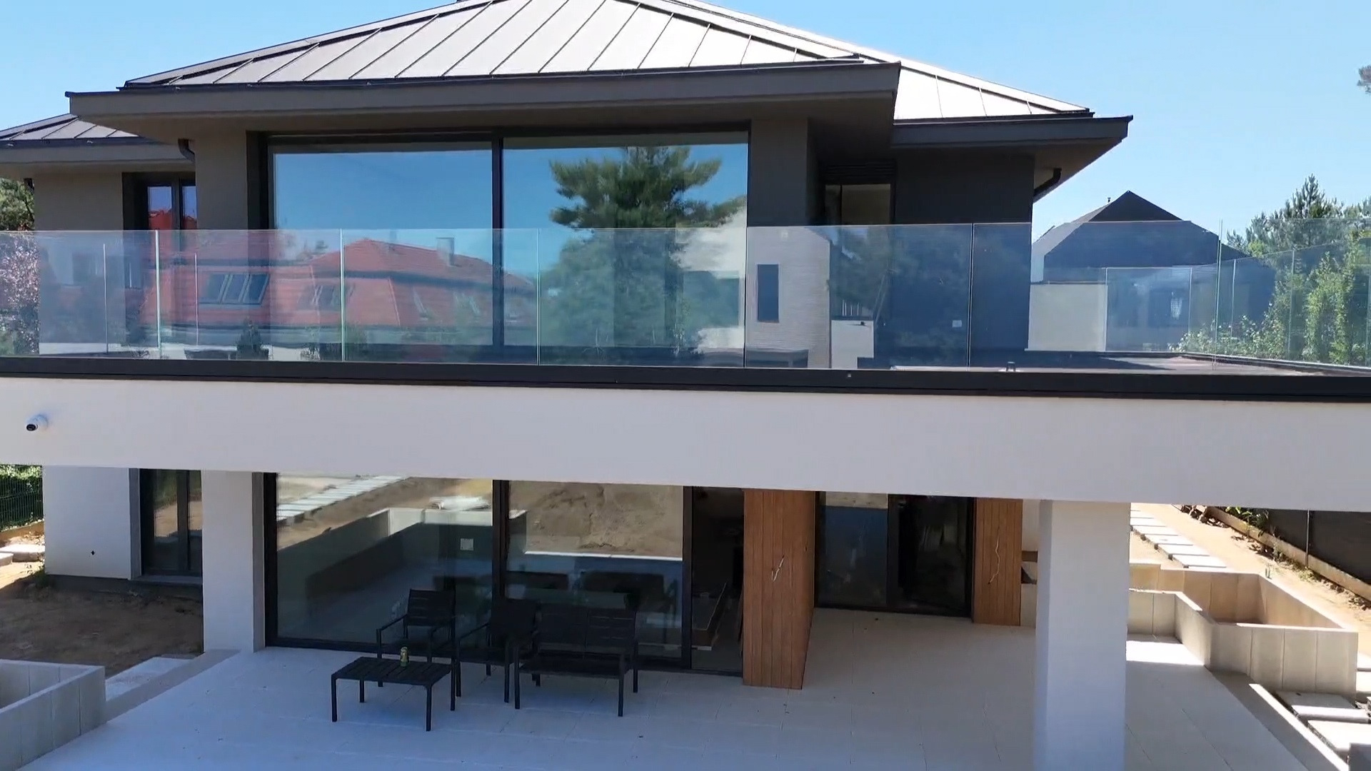 Nowoczesny dom z dużymi przeszkleniami i szklanymi balustradami na balkonie, widok z dołu, jasne tło.