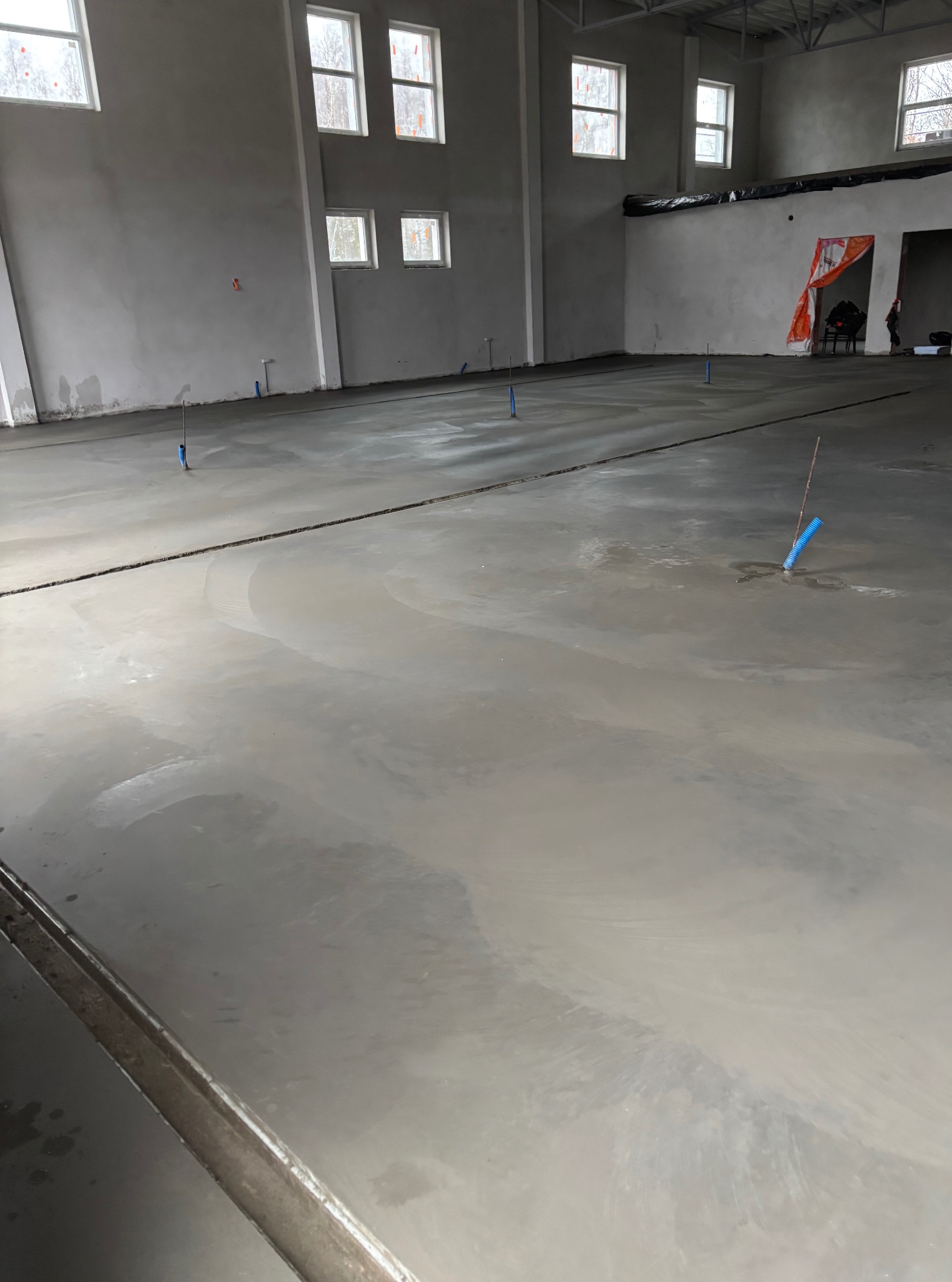 Wylana, świeża posadzka w hali przemysłowej z widocznymi znacznikami poziomów. W tle ściany z oknami i częściowo zakryty obszar roboczy.