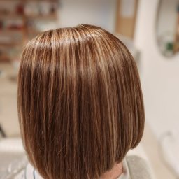 PRACOWNIA FRYZJERSKA ANITA DRATKOWICZ - Brązowe włosy z blond pasemkami, krótko obcięte w stylu bob, widoczne od tyłu, z delikatnym połyskiem i naturalnym światłem w tle.