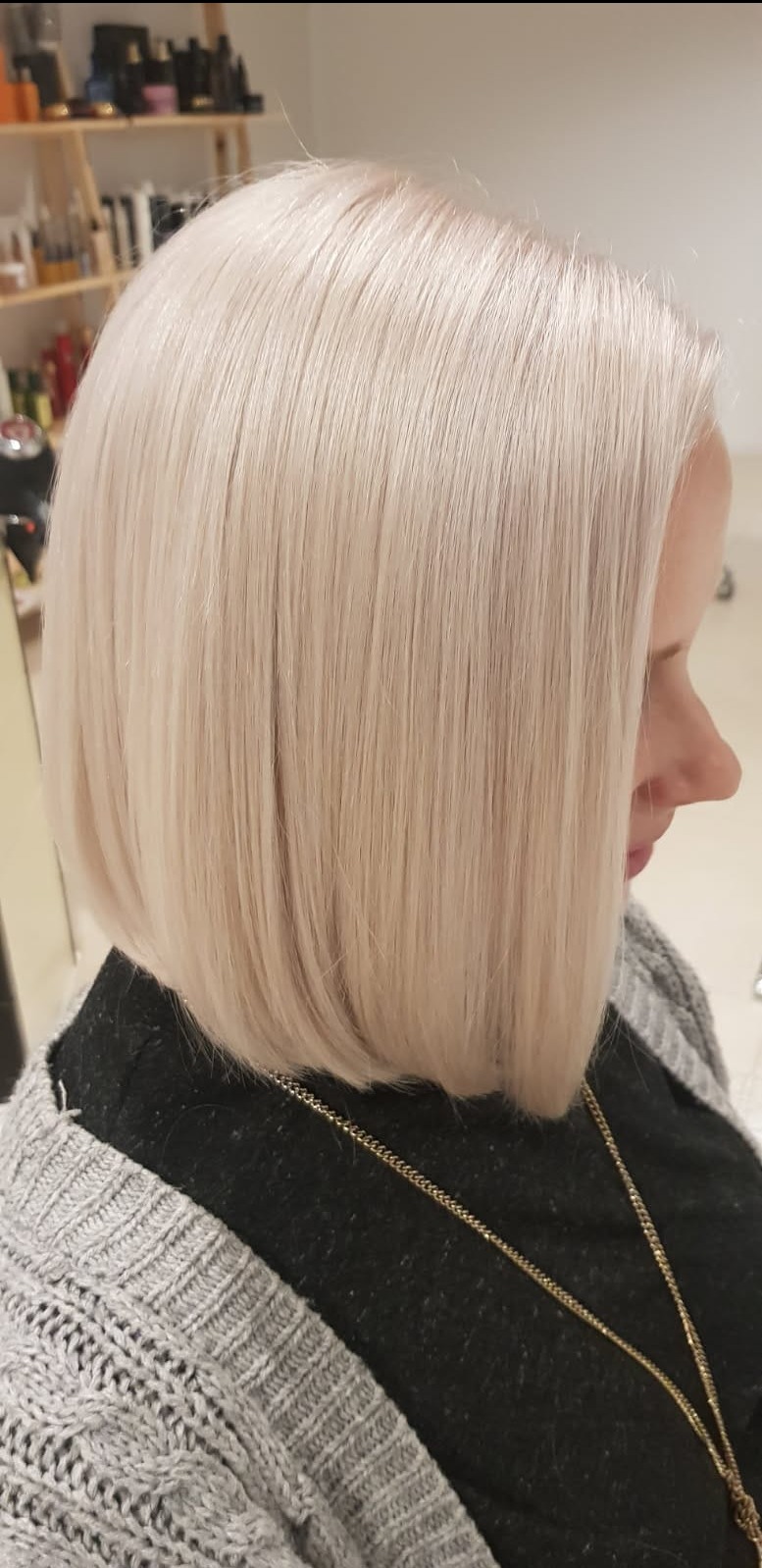 Platynowy blond bob z idealnie prostymi włosami, widok z boku. Damska fryzura po zabiegu koloryzacji i strzyżenia w salonie fryzjerskim.
