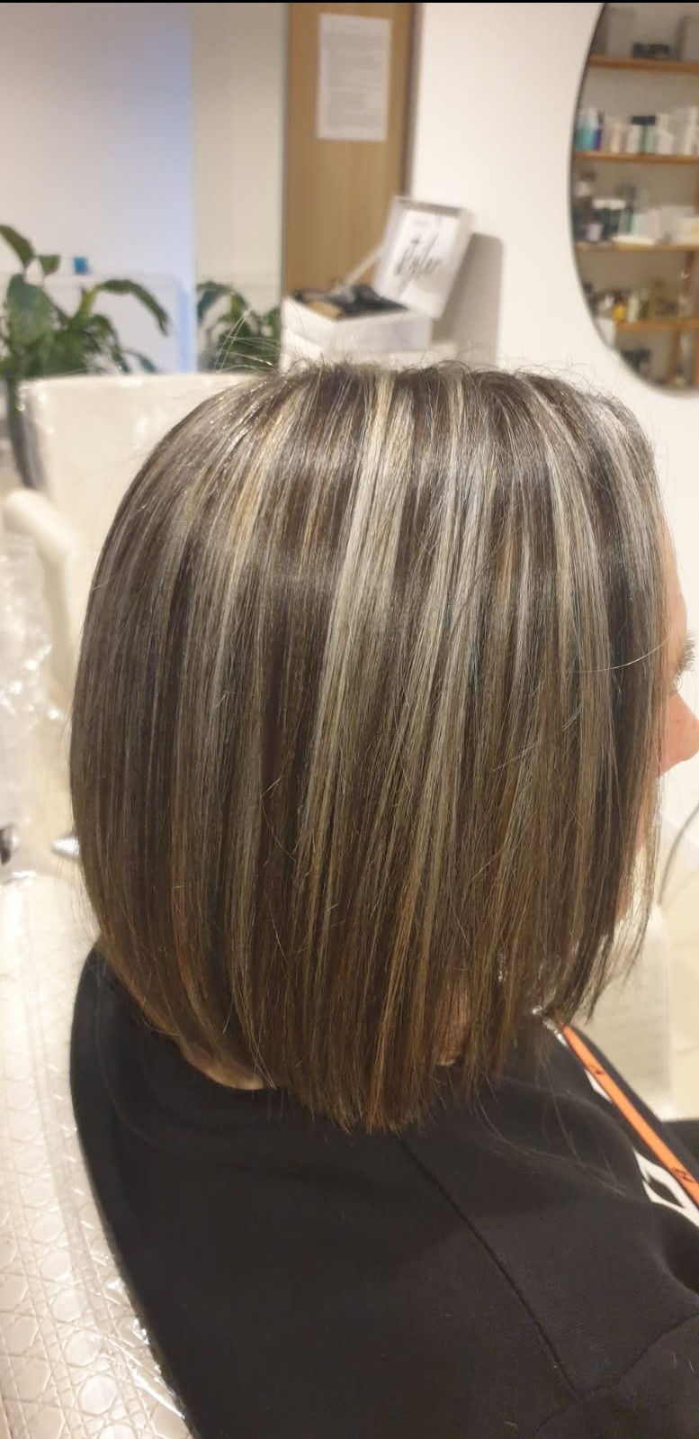 Uczesanie po koloryzacji: brązowe włosy z blond pasemkami, krótko obcięte w salonie fryzjerskim. Widok z boku, w tle lustro i kosmetyki.