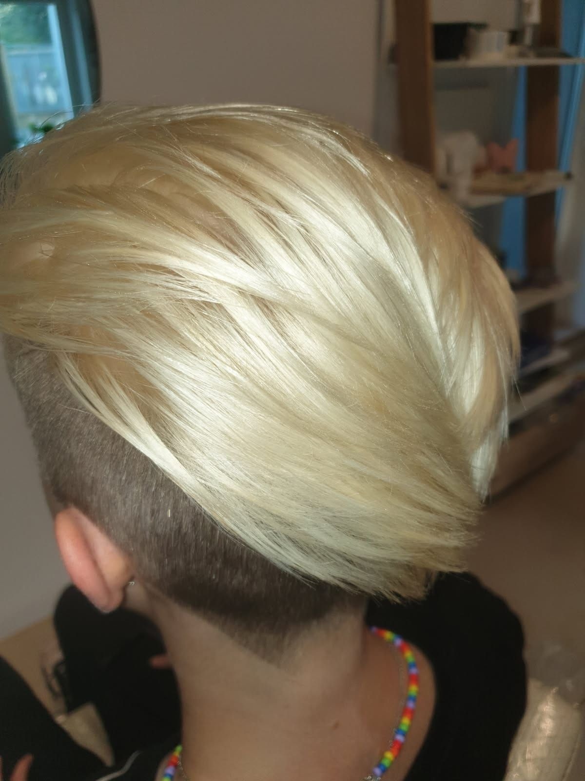 Blond włosy z krótkim bokiem i tyłem, widok z tyłu głowy. Włosy ułożone w fale, z widocznym cieniowaniem. Kolor włosów platynowy blond.