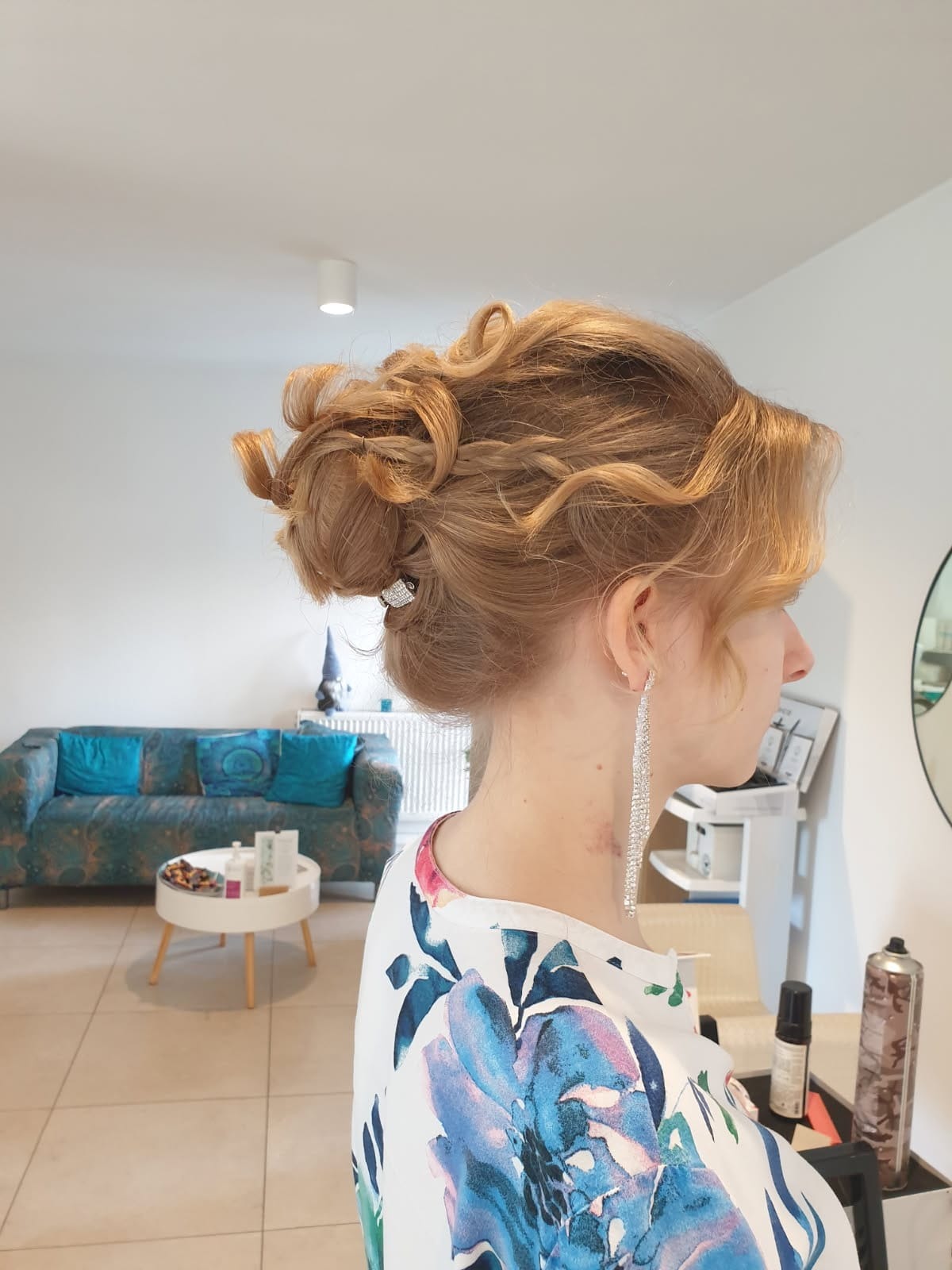 Upięcie ślubne z warkoczem i błyszczącą spinką, widok z profilu na jasnym tle salonu. Długie, srebrne kolczyki dodają elegancji.