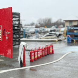 ProfiFire - Czerwona szafka hydrantowa z otwartymi drzwiczkami i kluczem, szereg gaśnic i wąż na zewnątrz w zimowych warunkach. Sprzęt ppoż na placu.