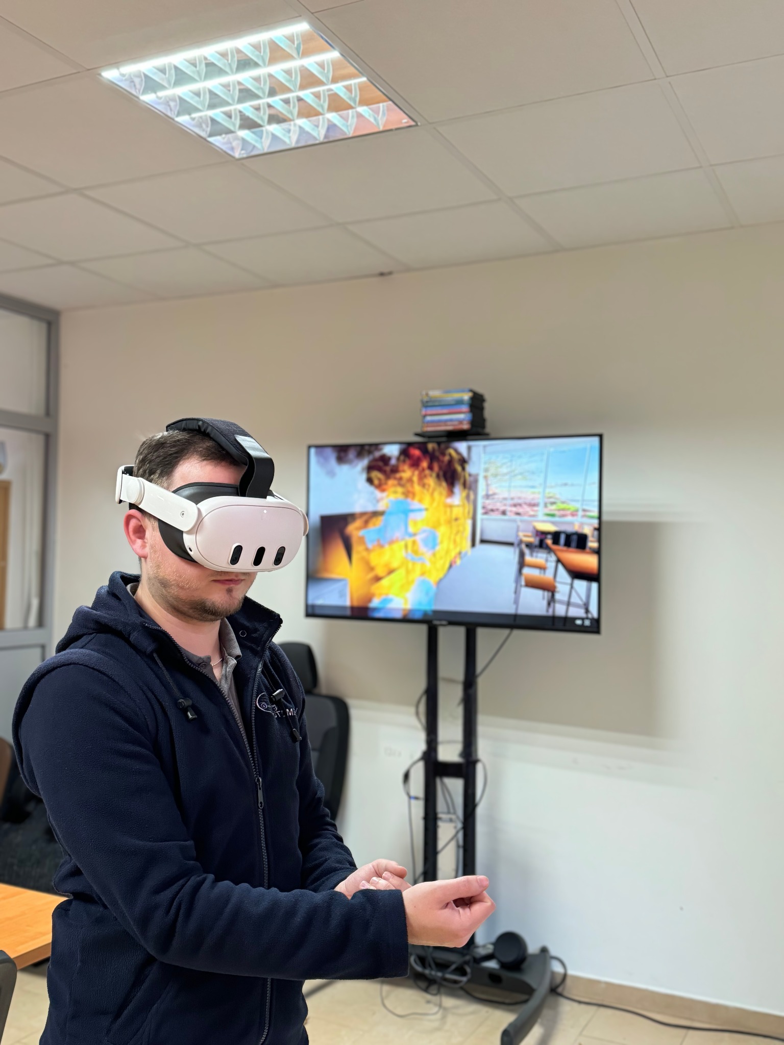 Mężczyzna w okularach VR uczestniczy w interaktywnym szkoleniu ppoż, symulacja pożaru widoczna na ekranie. Szkolenie w sali konferencyjnej.