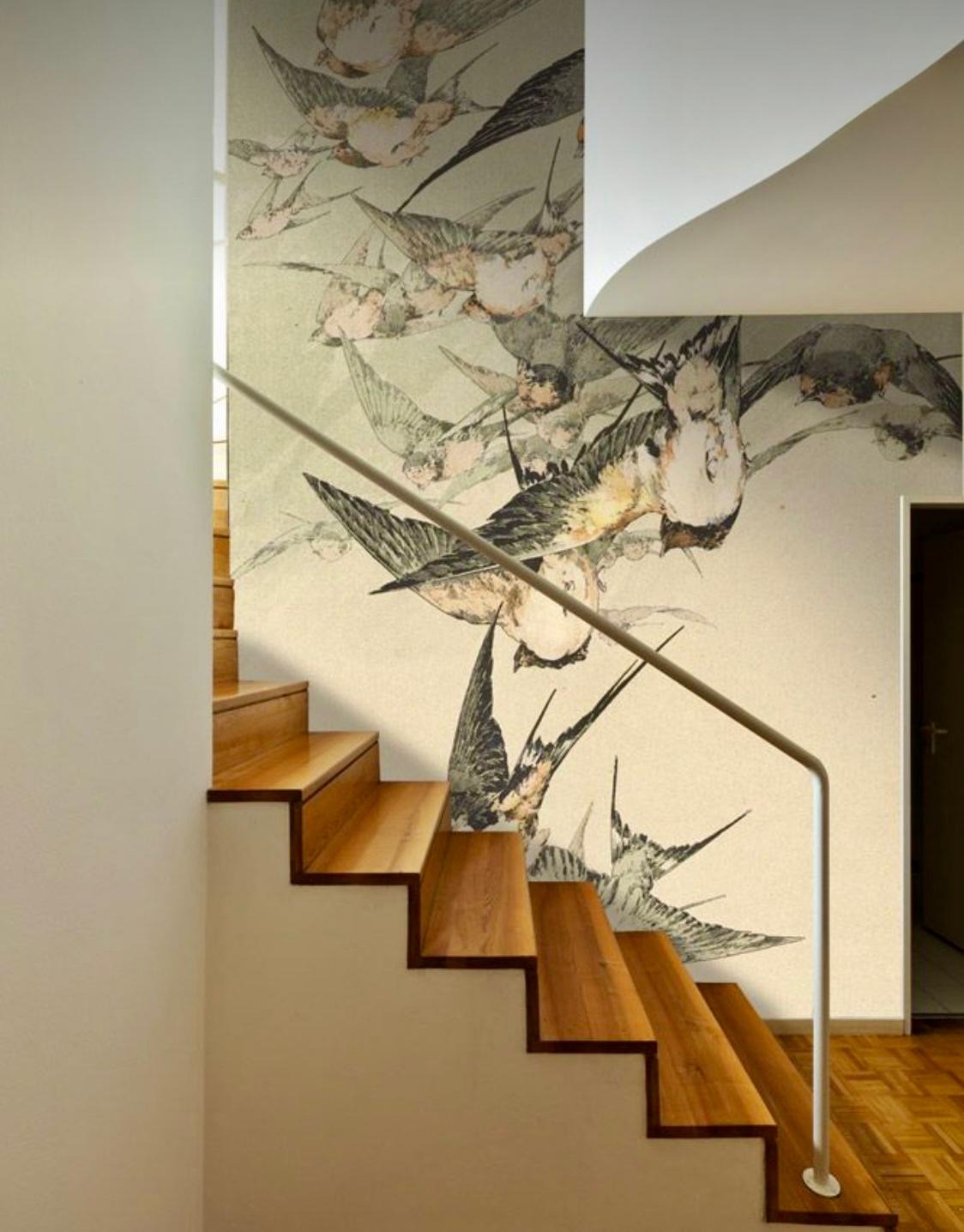 Ściana przy schodach z tapetą w ptaki, jasne drewniane schody i biała balustrada. Dekoracja wnętrza z motywem natury, artystyczne wykończenie.