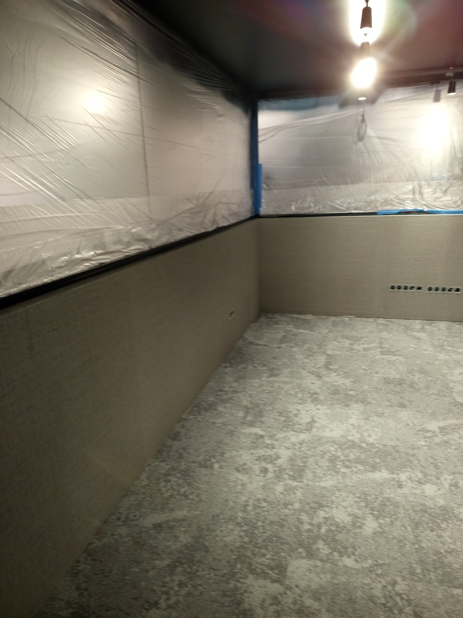 Pokój po odświeżeniu ścian, zabezpieczony folią malarską. Widoczne gładkie, szare ściany z poziomym wzorem i przygotowane otwory na gniazdka elektryczne.