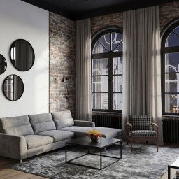Aneta Kwiatkowska Projektowanie Wnętrz - Loftowy salon z szarą sofą, ceglaną ścianą i okrągłymi lustrami. Widok na nocne miasto przez okna w stylu industrialnym. Czarny sufit z oświetleniem punktowym.