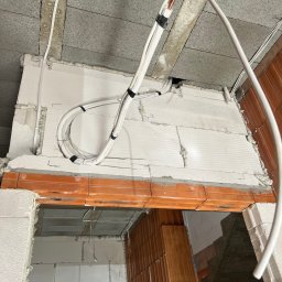ClimaNext Gen Adam Jochemczyk - Instalacja przewodów klimatyzacji w ścianie z betonu komórkowego, widoczne kable i rurki miedziane, etap prac instalacyjnych w nowym budynku.