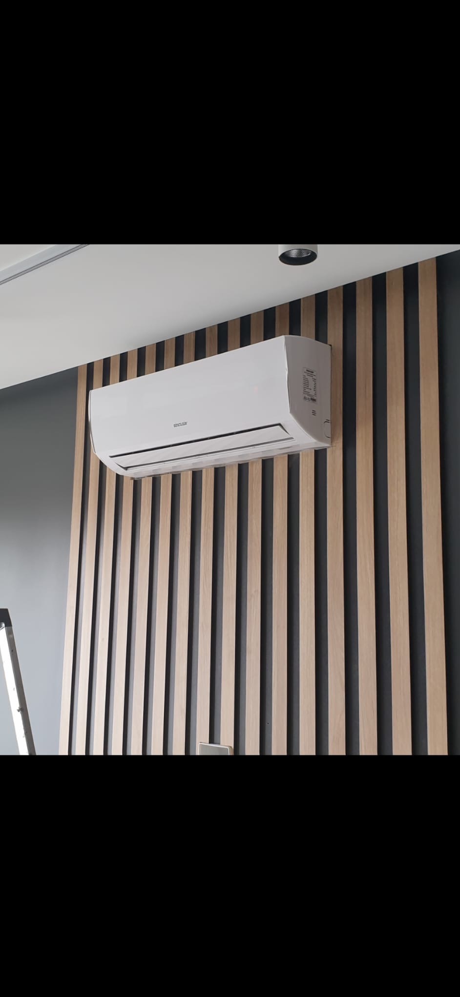 Biała klimatyzacja ścienna zamontowana na dekoracyjnej ścianie z drewnianych listew w nowoczesnym wnętrzu. Widoczny fragment drabiny.