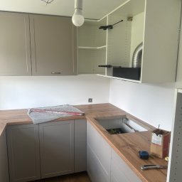 Bartosz Dąbek - Montaż szarych szafek kuchennych z drewnianym blatem. Widoczne narzędzia i akcesoria montażowe. Ujęcie z bliska na etapie instalacji.