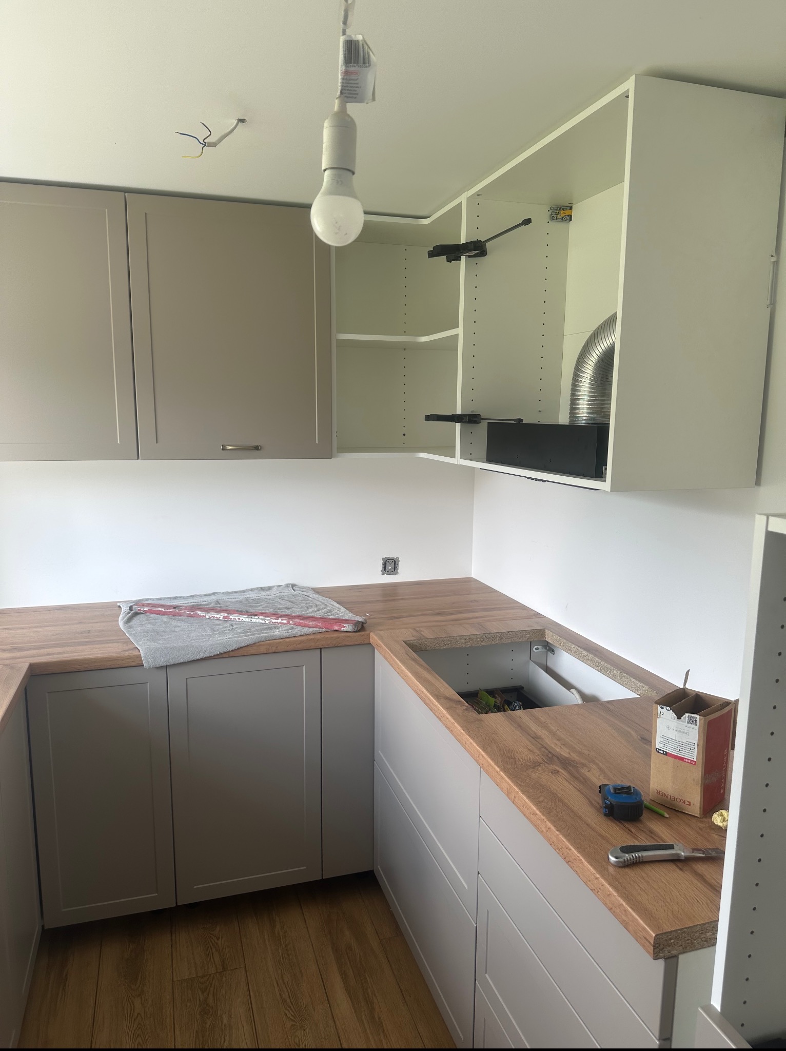 Montaż szarych szafek kuchennych z drewnianym blatem. Widoczne narzędzia i akcesoria montażowe. Ujęcie z bliska na etapie instalacji.