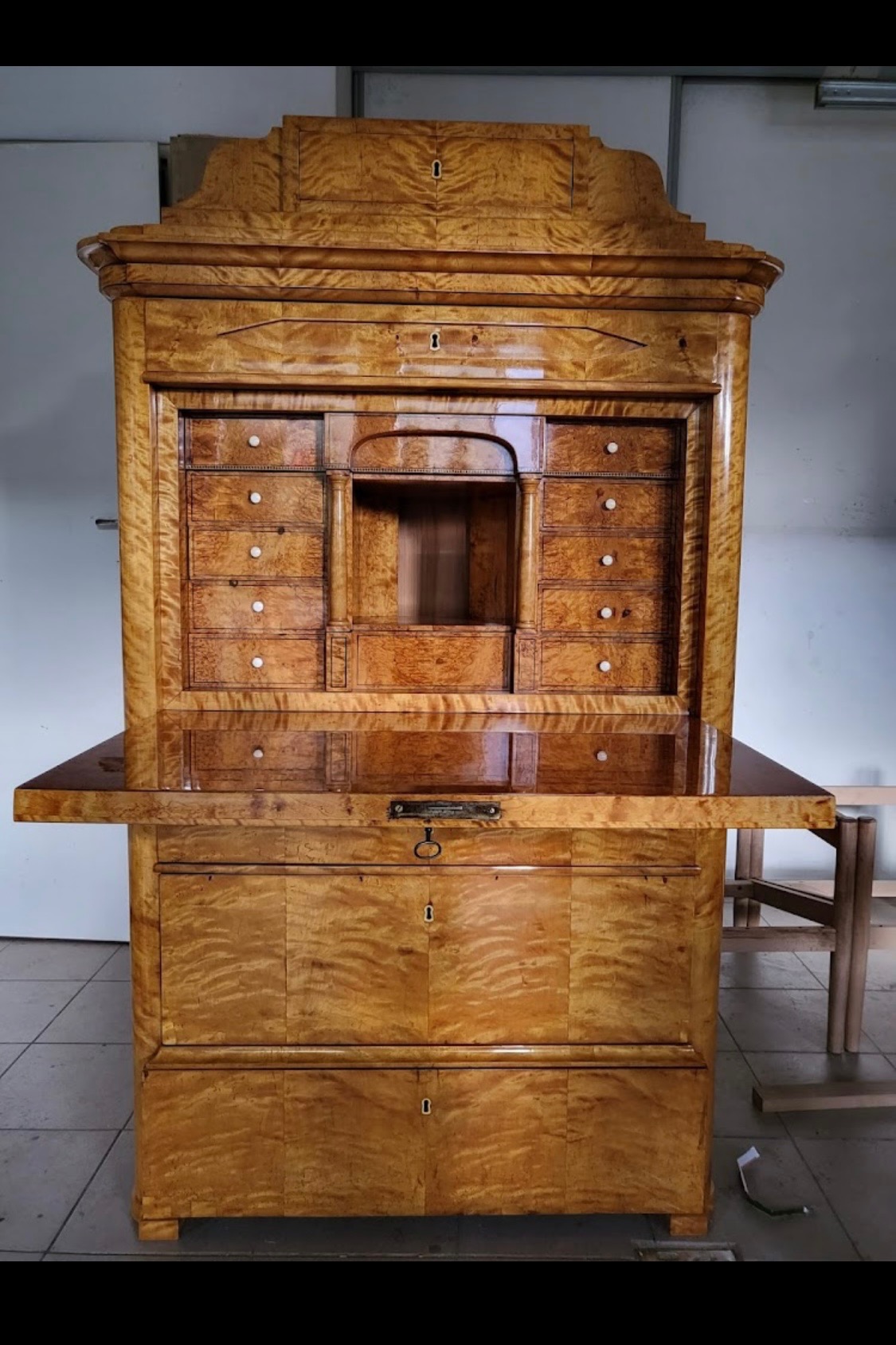 Antyczny sekretarzyk z drewna o unikalnym wzorze słojów, z otwartym blatem i licznymi szufladami, ukazujący kunsztowne detale i precyzję wykonania.