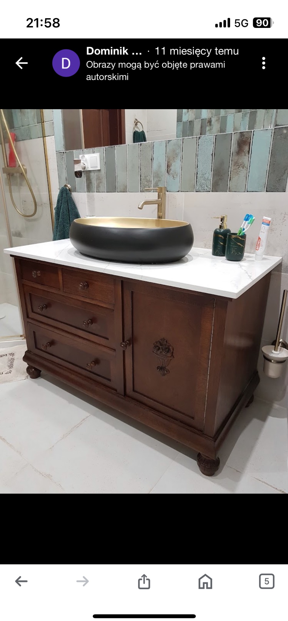 Stylowa, ciemnobrązowa szafka łazienkowa z marmurowym blatem i owalną umywalką w kolorze czarno-złotym. Widoczna armatura i akcesoria łazienkowe.