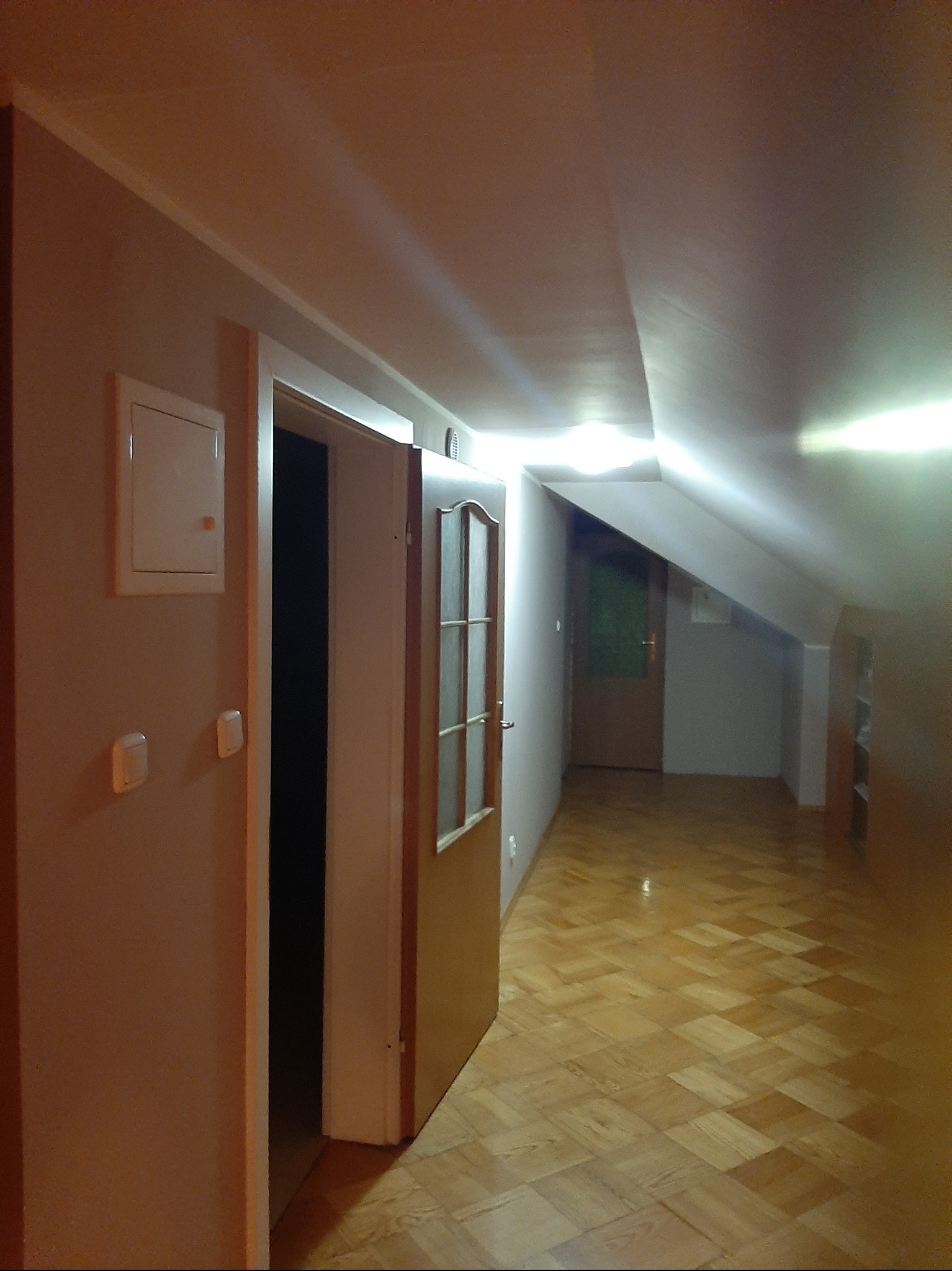 Poddasze po remoncie: świeżo pomalowane ściany w odcieniach beżu, odnowiona drewniana podłoga w jodełkę, nowe oświetlenie i drzwi z przeszkleniami.