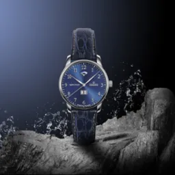 Elegancki, srebrny zegarek z niebieską tarczą 'Aqua Vigor' na skórzanym pasku, ustawiony na szarym kamieniu z efektem rozpryskującej się wody. Zdjęcie reklamowe produktu.