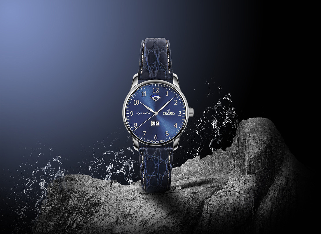 Elegancki, srebrny zegarek z niebieską tarczą 'Aqua Vigor' na skórzanym pasku, ustawiony na szarym kamieniu z efektem rozpryskującej się wody. Zdjęcie reklamowe produktu.