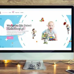 Ekran komputera wyświetla stronę sklepu internetowego KidsShop.pl z zabawkami dla dzieci. W tle drewniana ściana i świąteczne dekoracje, tworzące przytulny nastrój.
