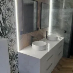 Nowoczesna łazienka z dwoma umywalkami na blacie z szufladami, podświetlanymi lustrami i wzorzystą tapetą w tropikalne liście.