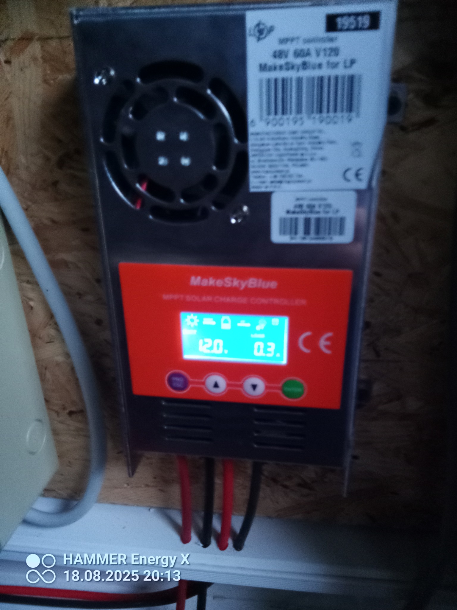 Kontroler ładowania solarnego MakeSkyBlue z wyświetlaczem wskazującym 12.0V i 0.3A, zamontowany na ścianie z boazerią. Widoczne kable i wentylator chłodzący.