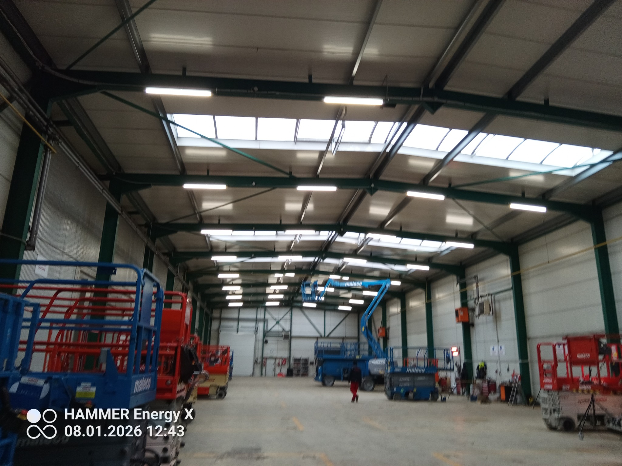 Hala magazynowa z oświetleniem przemysłowym w Gdyni. Widoczne podnośniki koszowe i świetliki dachowe.