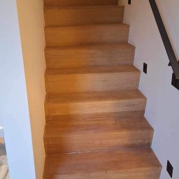 SŁOWIK INTERIORS - Maciej Słowik - Drewniane schody z metalową poręczą, oświetlone punktowymi lampami na ścianie. Widoczne detale wykończenia i naturalna barwa drewna.