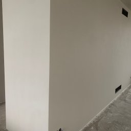 SŁOWIK INTERIORS - Maciej Słowik - Ściana po obróbce w Ząbkach: gładka powierzchnia z widocznymi otworami wentylacyjnymi, przygotowana do dalszych prac wykończeniowych. Minimalistyczny kadr.