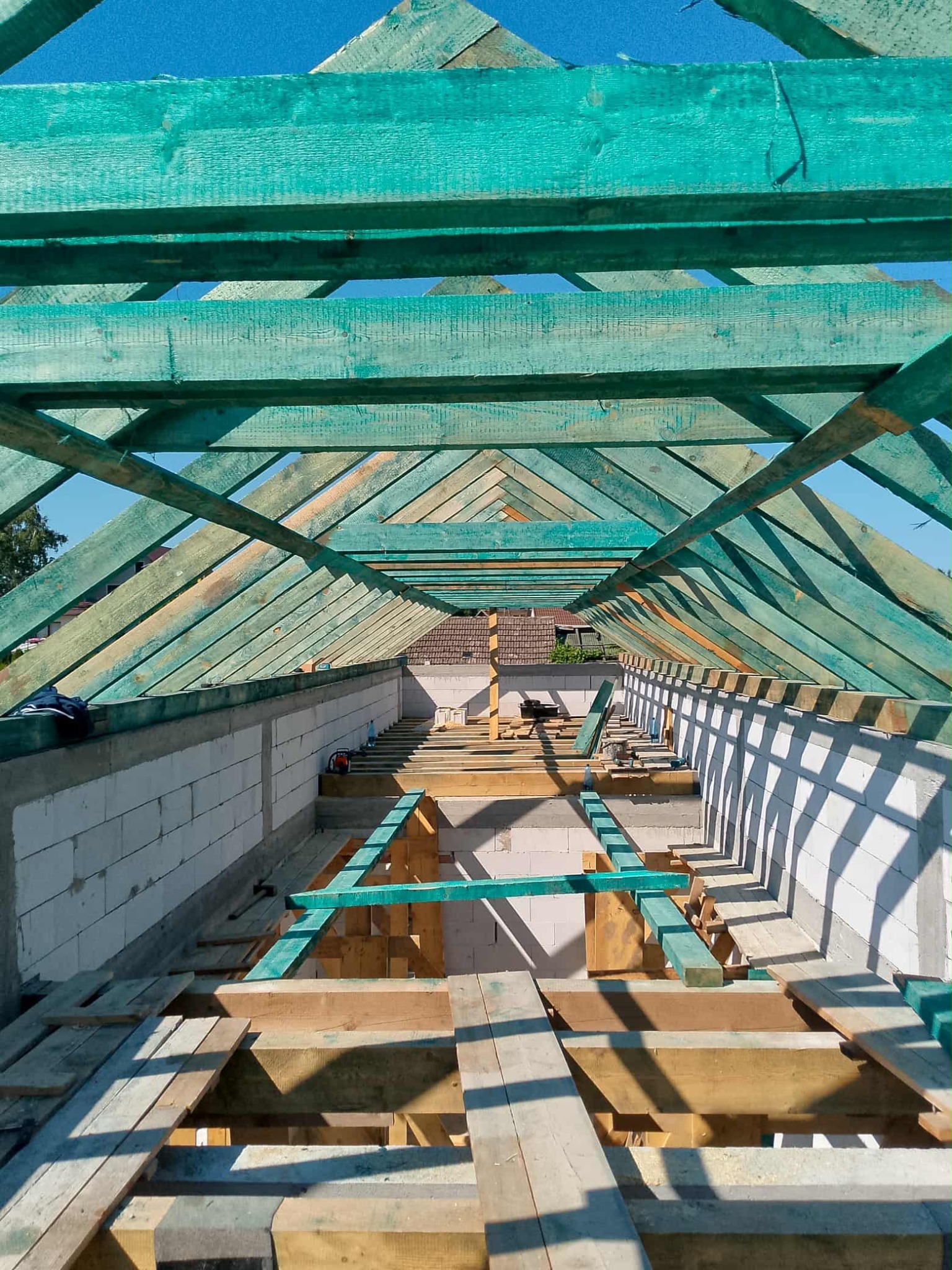 Wnętrze budowy dachu z impregnowaną na zielono drewnianą konstrukcją, widok z dołu ukazujący perspektywę i materiały budowlane.