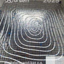 ARSEM sp z o.o. klimatyzacja, chłodnictwo, pompy ciepła, rekuperacja, wentylacja - Białe rury ogrzewania podłogowego ułożone spiralnie na czarnej siatce, zabezpieczone niebieskimi klipsami. Widoczny napis 'arsem' i rok '2025'.