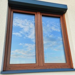 Adam Frankiewicz BŁYSK - ZYSK - Czyste okno z brązową ramą i roletą w Lidzbarku odbija błękitne niebo z chmurami. Świeżo umyte okno w elewacji budynku. Widok z zewnątrz, jasne światło.