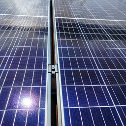 Adam Frankiewicz BŁYSK - ZYSK - Błyszczące panele fotowoltaiczne z widocznymi odbiciami światła i kroplami wody, zamontowane na metalowej konstrukcji. Widok z bliska, ukazujący detale.