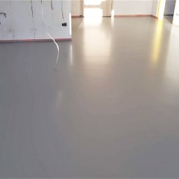 InterioDecor - dekoracyjne posadzki żywiczne - Szara, gładka posadzka w jasnym wnętrzu z przygotowanymi ścianami do malowania. Widoczne kable i taśmy zabezpieczające. Minimalistyczny design.