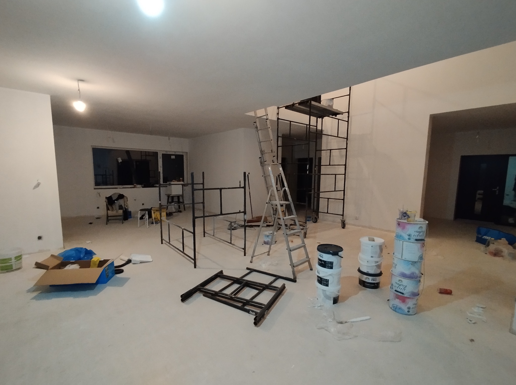 Wnętrze w trakcie malowania: puste puszki po farbie, drabina, rusztowanie, elementy mebli. Przygotowanie do malowania ścian w jasnym, przestronnym pomieszczeniu.