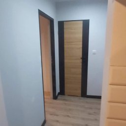 P.P.H.U. GLOB3. RAFAŁ GUGUŁA - Nowoczesne drzwi wewnętrzne z ciemną ościeżnicą i drewnianym wypełnieniem, zamontowane w korytarzu w Rudzie Śląskiej. Widoczna podłoga imitująca drewno.