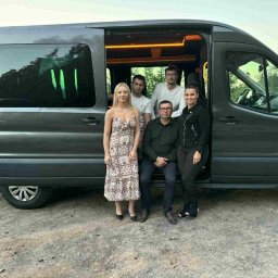 EASYROAD - przewozy międzynarodowe - Grupa pięciu osób pozuje przy otwartym, szarym busie z podświetlanym wnętrzem. Widoczne drzewa w tle. Ujęcie z boku, na zewnątrz pojazdu.