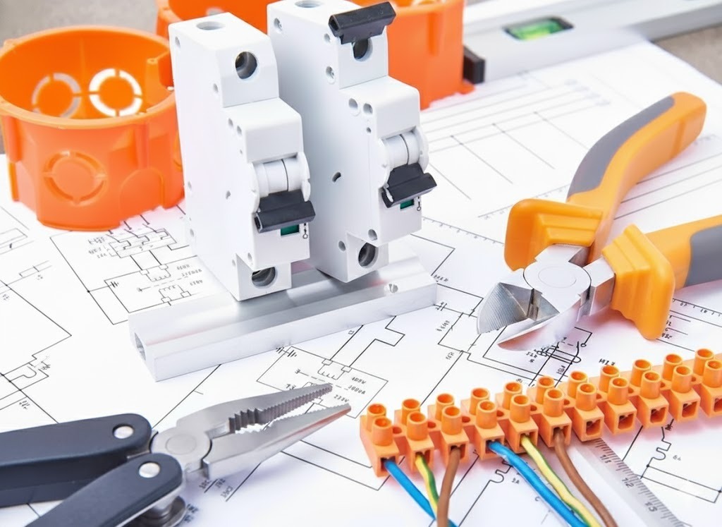 Schemat elektryczny z wyłącznikami, puszką instalacyjną, złączką, kombinerkami i szczypcami, ukazujący etap prac instalacyjnych w jasnym oświetleniu.