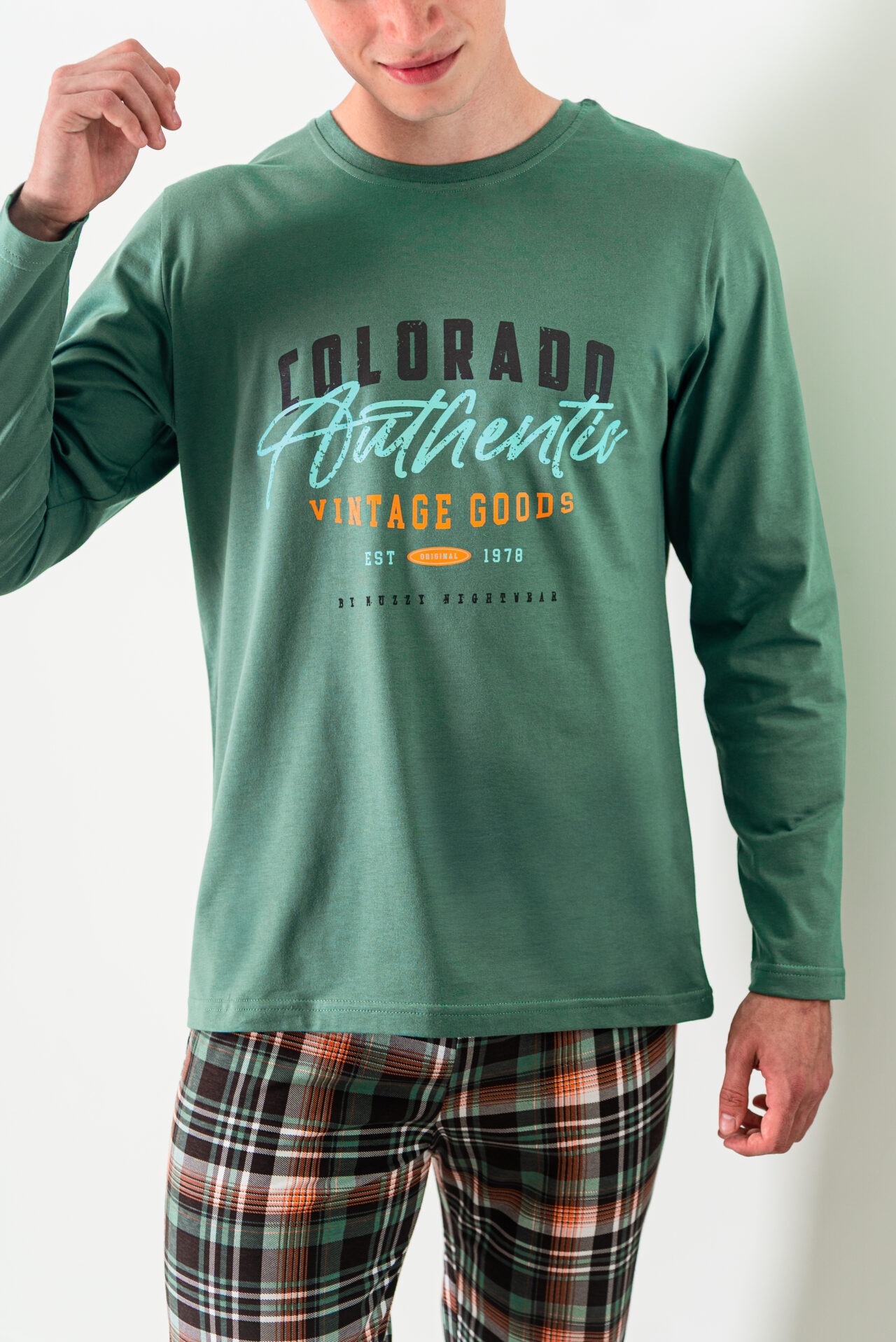 Męska piżama: zielona koszulka z długim rękawem i nadrukiem 'Colorado Authentic Vintage Goods' oraz spodnie w kratę. Częściowo widoczna postać na białym tle.