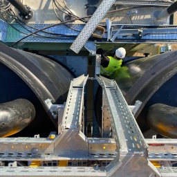 VoltEco usługi elektryczne Patryk Kubulus - Praca na wysokości: instalacja korytek kablowych i rur na konstrukcji zbiornika. Pracownik w kasku i kamizelce odblaskowej. Widok z góry, ostre światło.