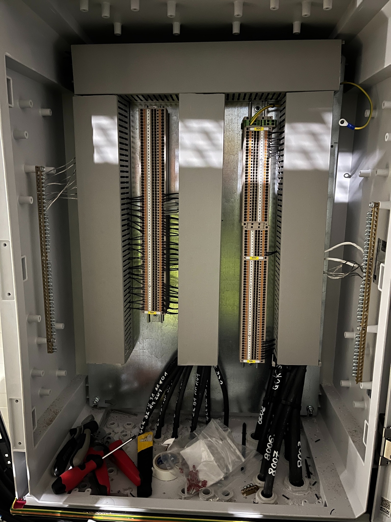 Rozdzielnica elektryczna w trakcie montażu: widoczne listwy zaciskowe, przewody z oznaczeniami i narzędzia. Wnętrze skrzynki rozdzielczej z elementami instalacji.