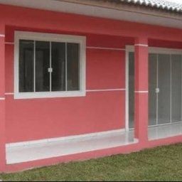 JS BRASIL - Różowa elewacja domu z białymi akcentami: okno z kratami i przeszklone drzwi balkonowe. Świeżo pomalowana ściana i podłoga balkonu. Widok z zewnątrz na trawnik.